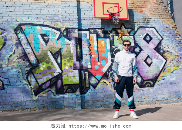 站在涂鸦墙和篮球框下的男人时尚的年轻男子在老式服装在砖墙前的涂鸦和篮球戒指